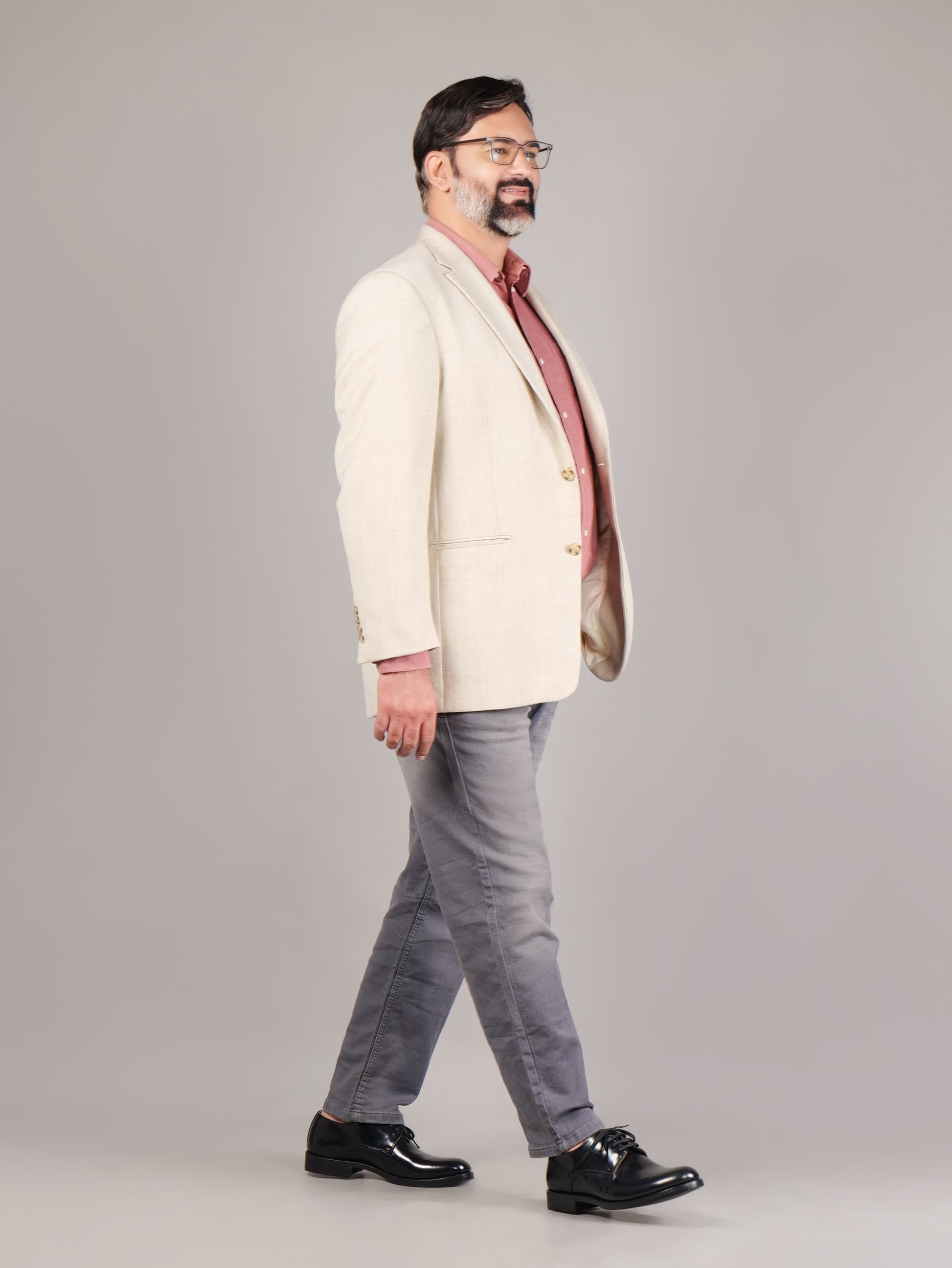 Man wearing a cream blazer, red shirt, gray pants, and black shoes on a plain background