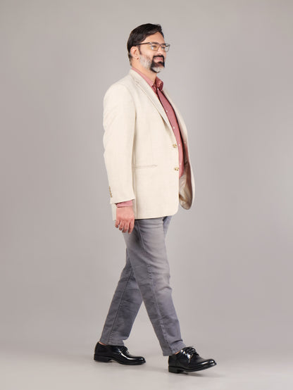 Man wearing a cream blazer, red shirt, gray pants, and black shoes on a plain background